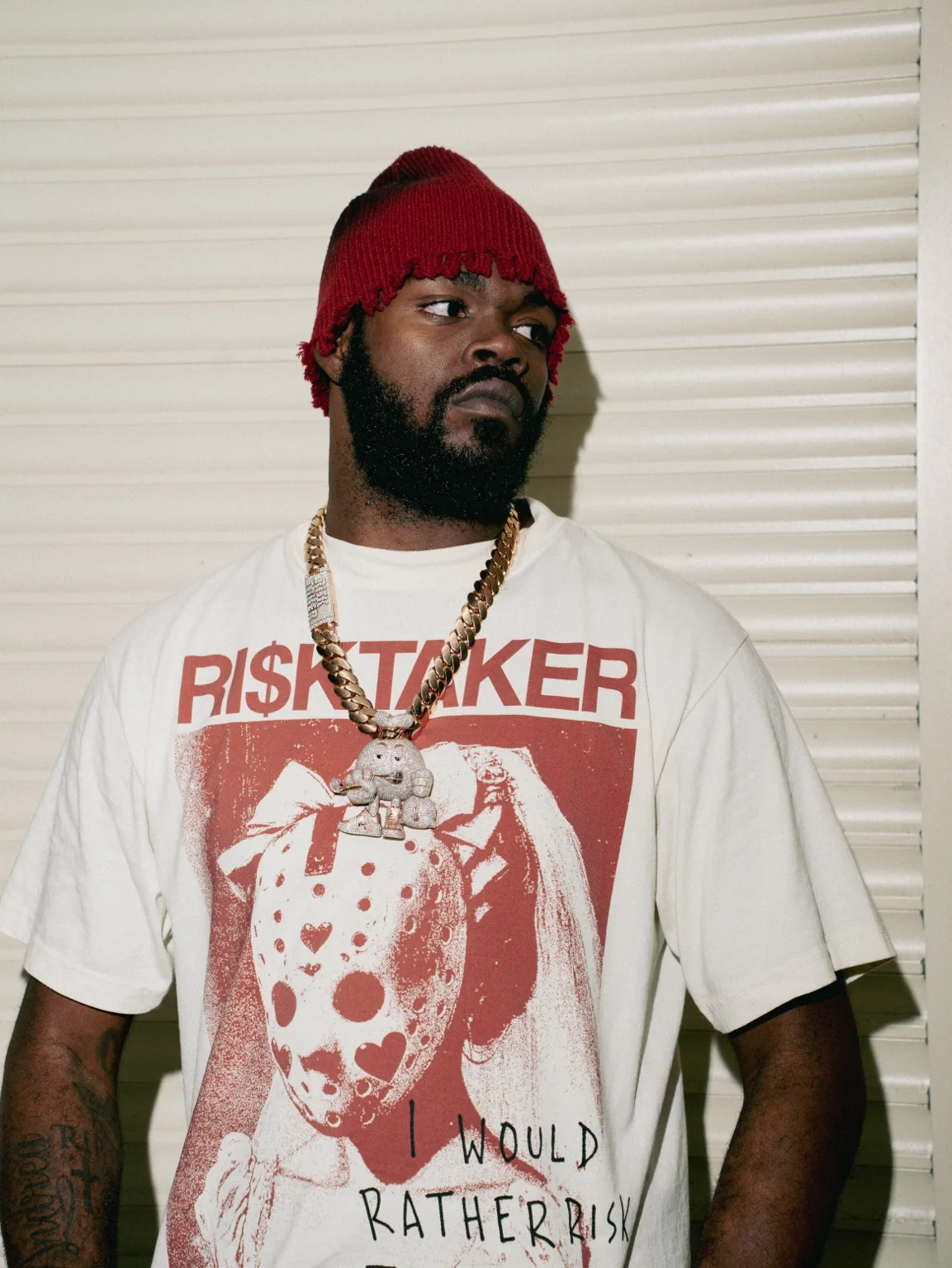 RI$KTAKER founder wearing the cream Mask Tee and oxblood red beanie in a close-up portrait